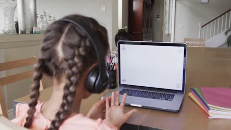 Biracial girl learning online at table using laptop with copy space on screen, slow motion