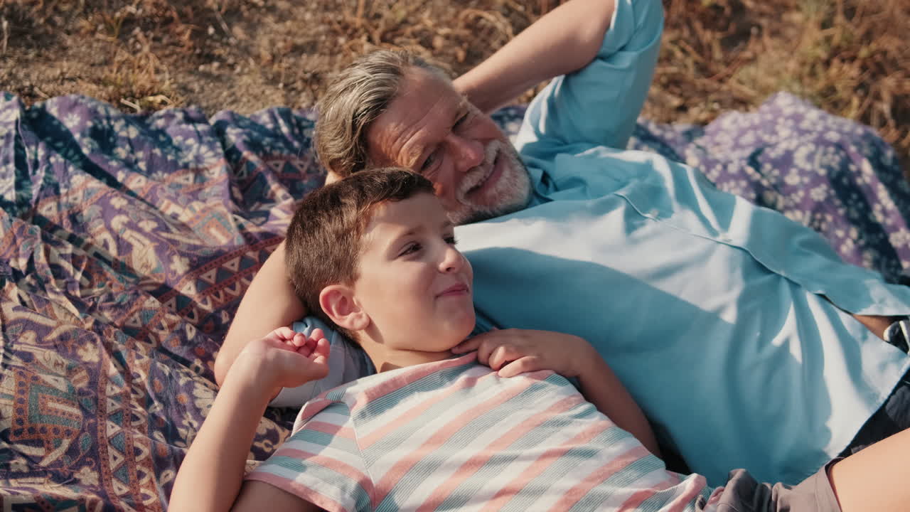 Nonno e nipote felici che si rilassano insieme su una coperta all'aperto