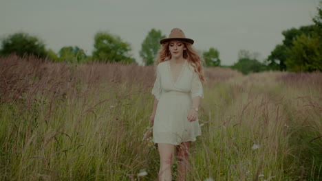 attractive boho woman walking on a meadow in summer holding flowers in hand