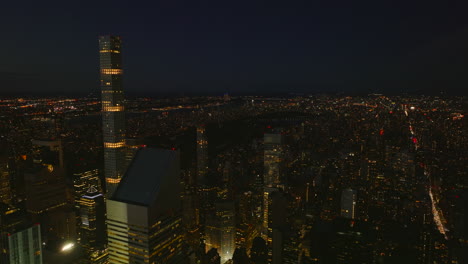 Descending-footage-of-illuminated-tall-office-towers-in-city.-Night-cityscape-in-background.-Manhattan,-New-York-City,-USA