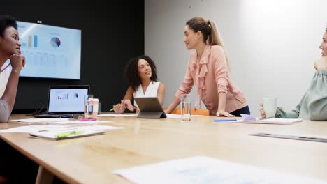 Diverse-businesswomen-having-presentation-at-office-meeting,-using-laptop-and-tablet,-in-slow-motion