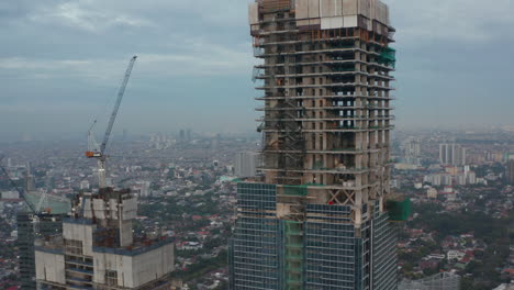 Close-up-aerial-shot-of-skyscraper-bare-skeleton-frame-under-construction-in-Jakarta,-Indonesia