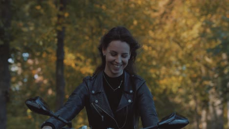 pretty smiling european young woman driving a motorbike wearing leather jacket in forest with vibrant, colorful golden autumn leaves on sunny day-5