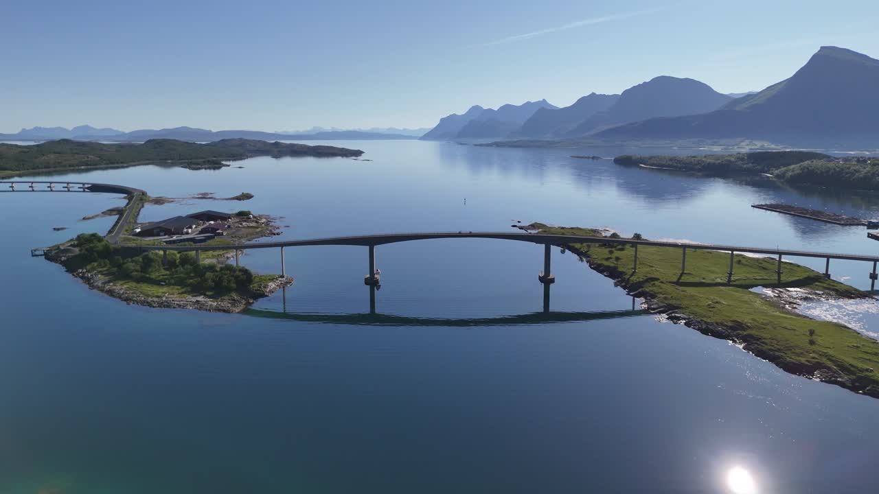 Beautiful drone footage of Engeløya island showing two bikers on a bridge, fjord reflections, and dramatic mountain landscape