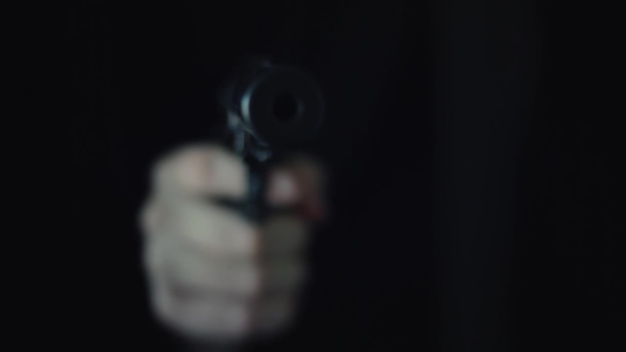 Unrecognizable assasin hitman with a silencer supressed silenced gun appearing from the shadows