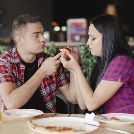 two people are eating one slice of pizza in the cafe. loving couple is enjoying pizza together