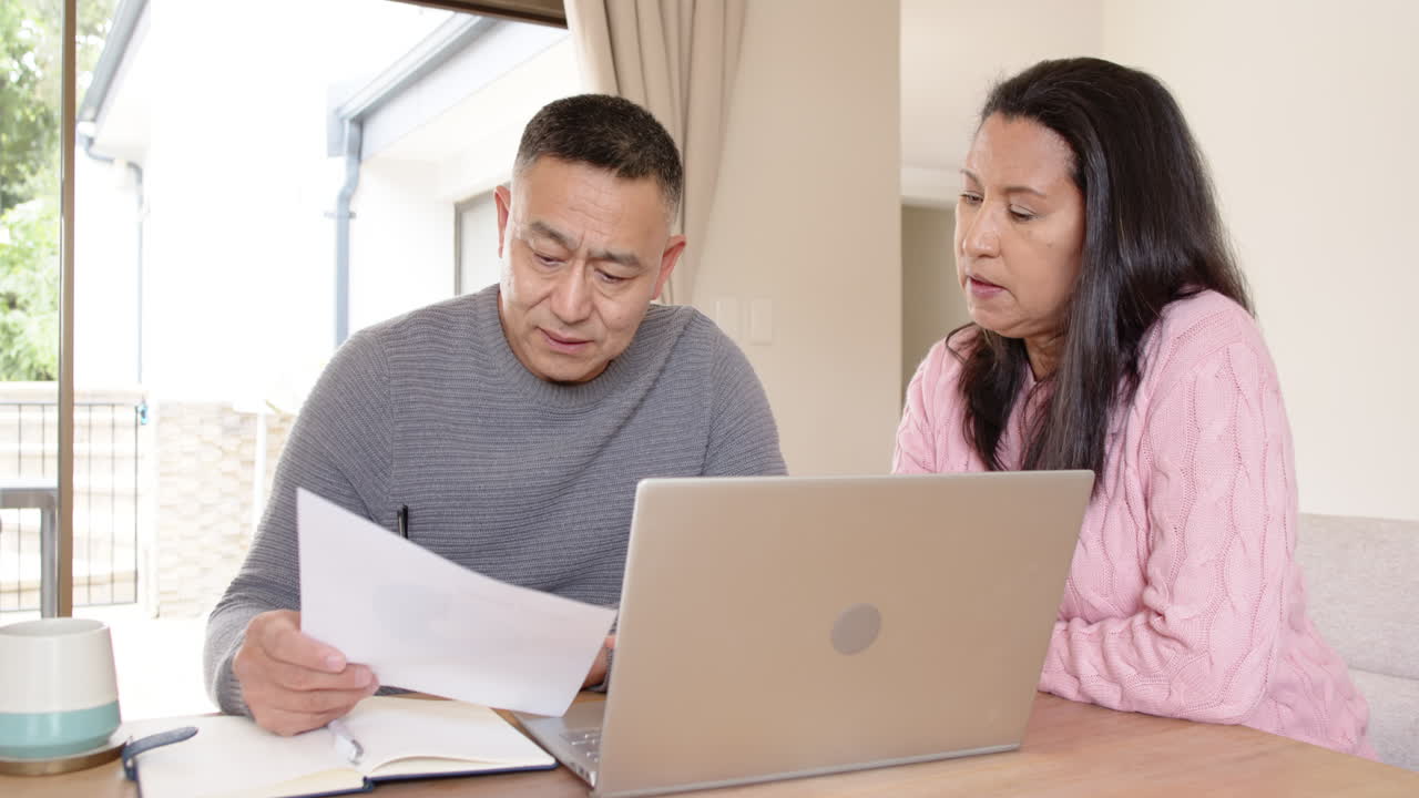 Senior asian couple reviewing documents together at home with laptop and coffee