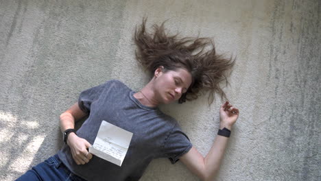 a gentle scene of a woman lying on the ground, holding a love letter on her stomach, as the camera slowly zooms out and rotates around her.