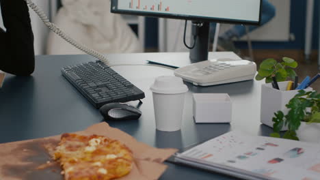 Closeup-of-businesswoman-sitting-at-desk-in-front-of-computer-eating-pizza-slice