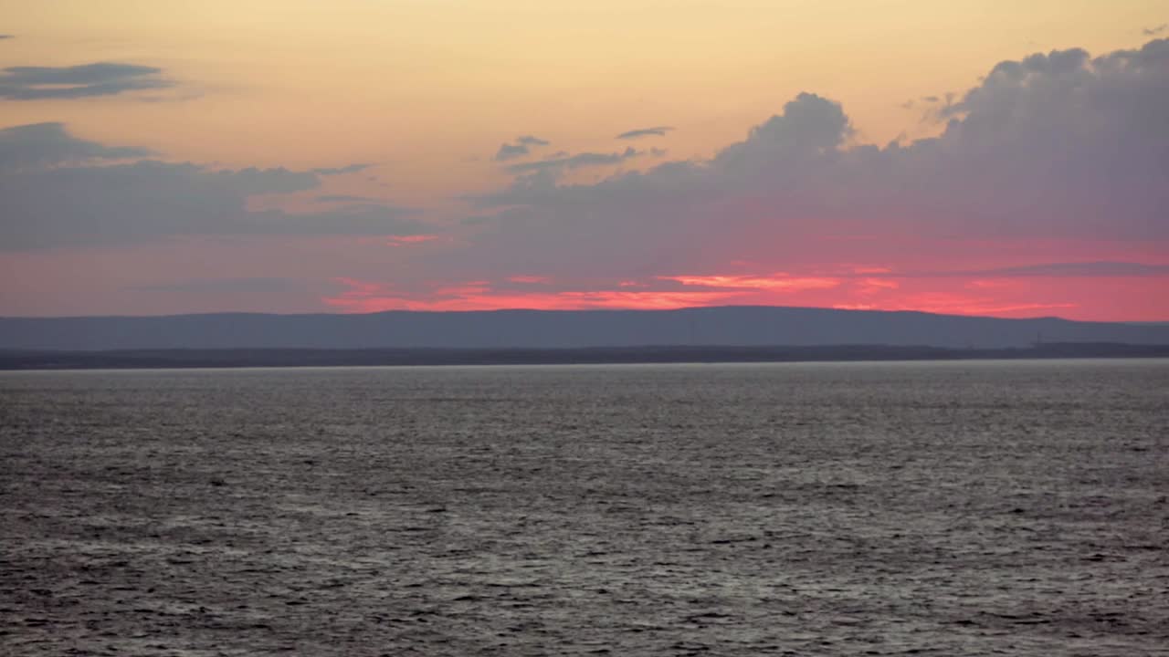vista desde el mar de la puesta de sol detrás de las nubes y las colinas cerca de sydney, nova scotia con faro parpadeando en la orilla