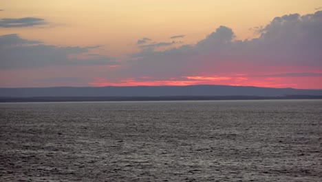 view from sea of sun setting behind clouds and hills near sydney, nova scotia with beacon flashing on shore