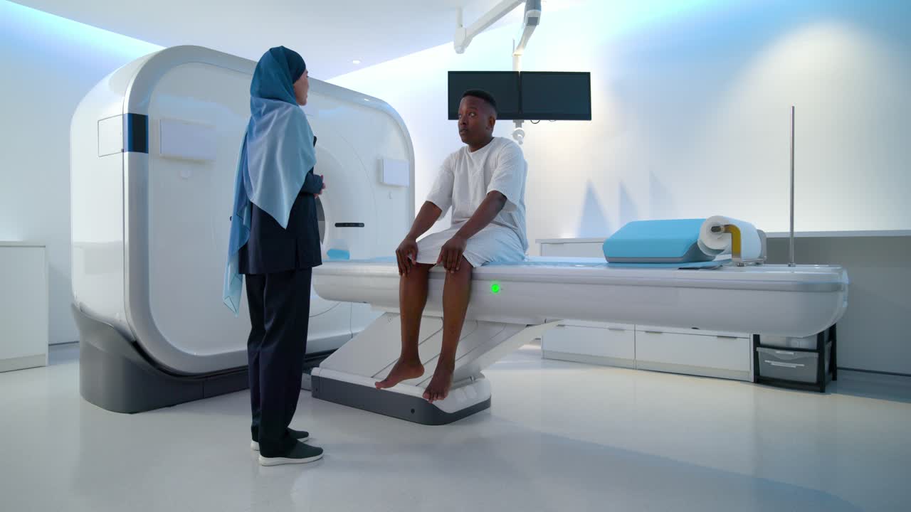 Medico afroamericano in piedi accanto allo scanner, che usa un tablet e guida il paziente mentre si prepara per la scansione