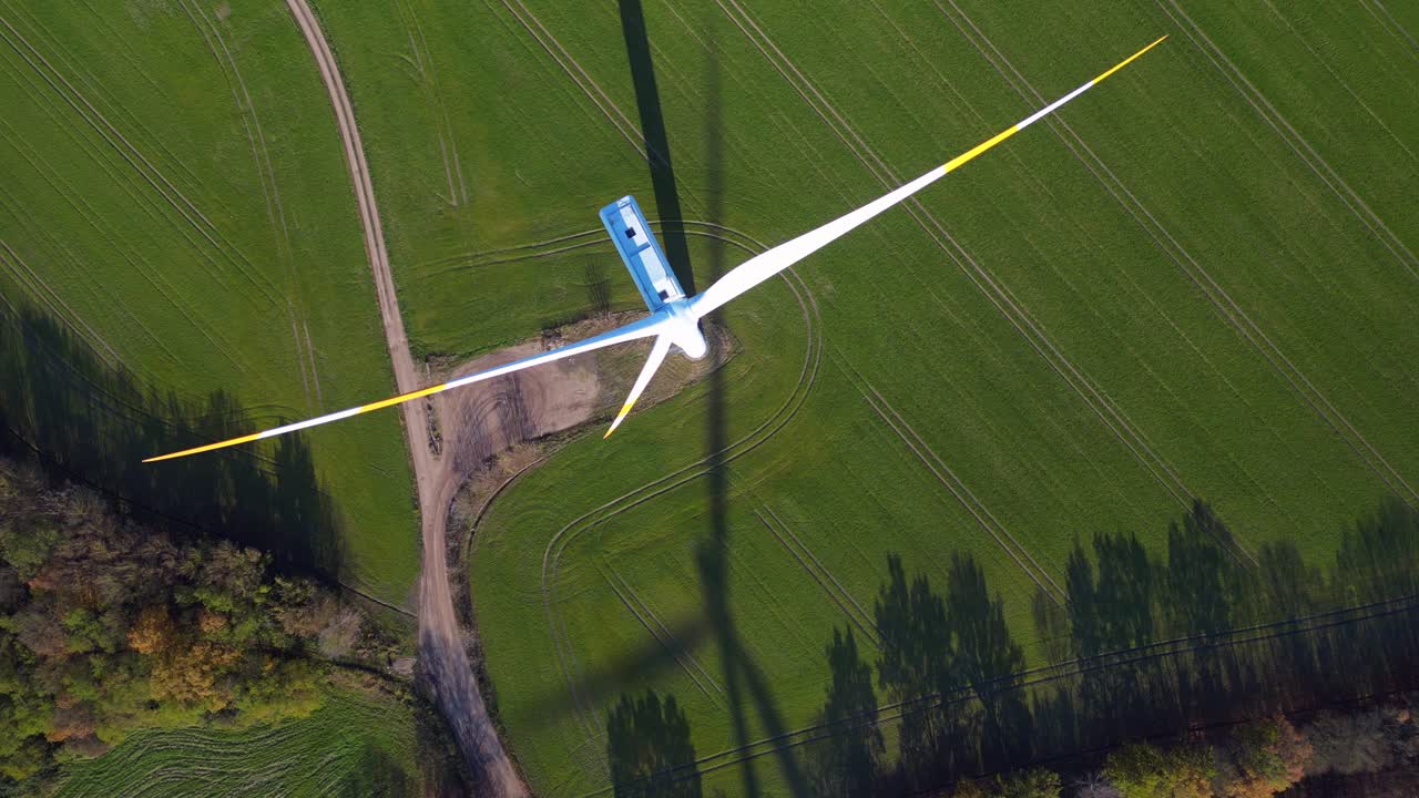 Wind turbine standing in green field next to highway autobahn in autumn Germany, generating renewable energy. Magic aerial view flight vertical bird's eye view drone