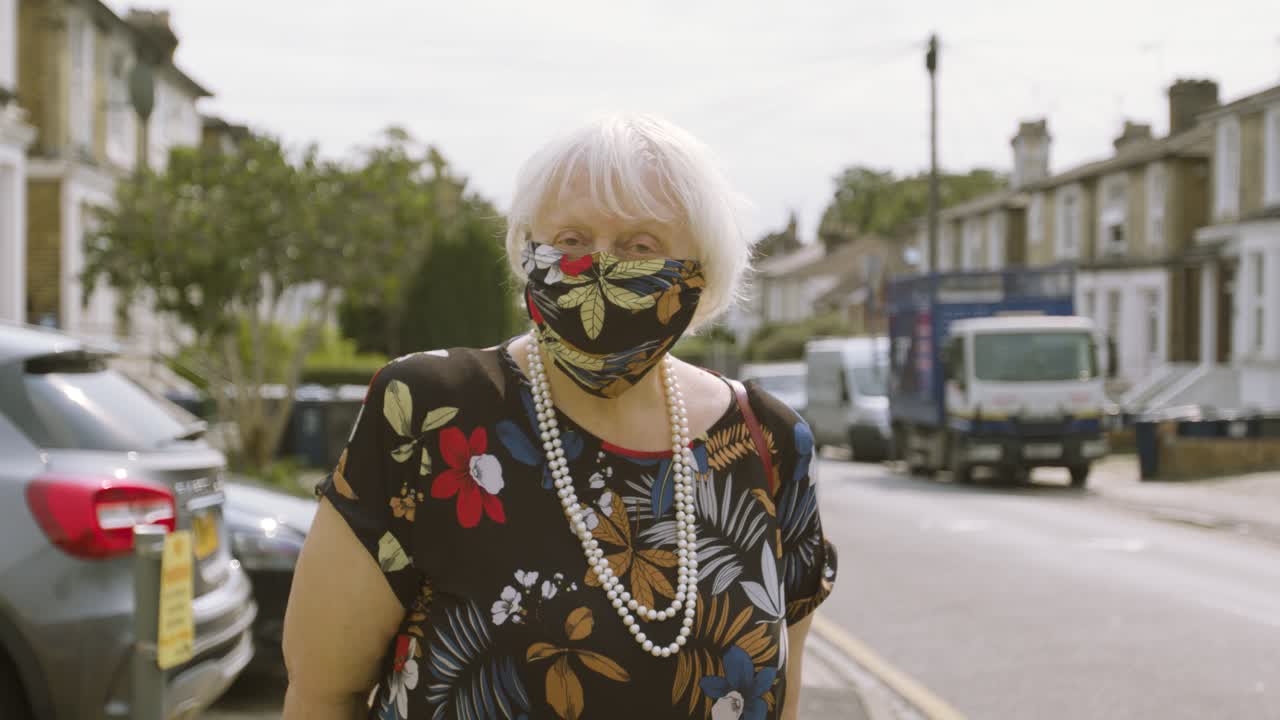 머리를 움직이는 카메라를 바라보며 일치하는 드레스와 얼굴 마스크를 쓴 노인 여성