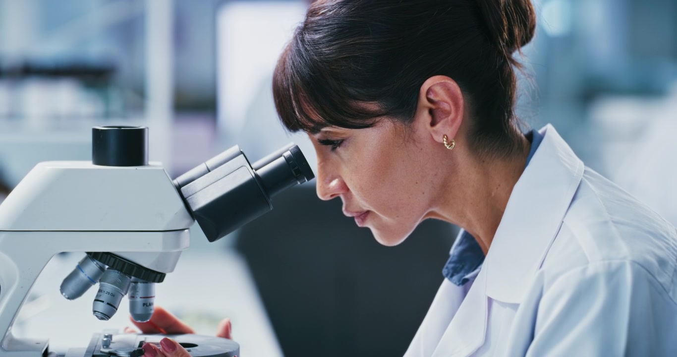 Scienziata che scrive appunti e usa il microscopio in laboratorio