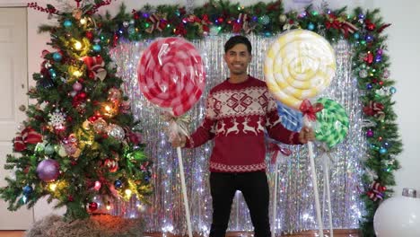 hombre feliz sosteniendo dos piruletas gigantes en un estudio decorado con temática navideña