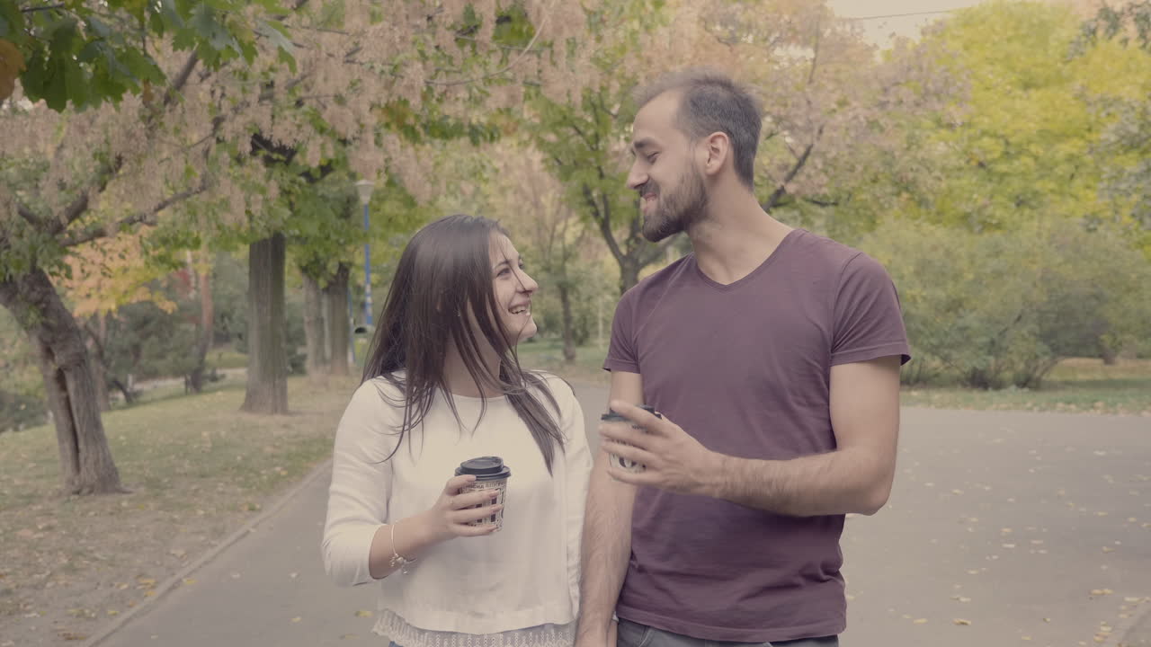 Pareja paseando por el parque con café