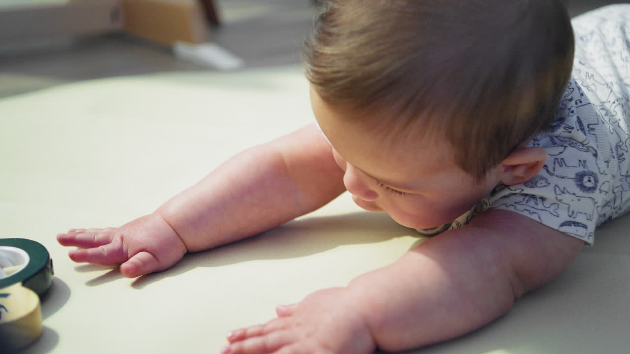 Bambino che sorride a terra, a pancia in giù, mentre impara a gattonare