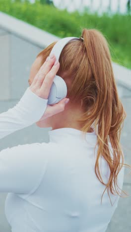 a sporty woman preparing for a workout by adjusting her headphones in a bright outdoor setting, emphasizing focus and energy in fitness