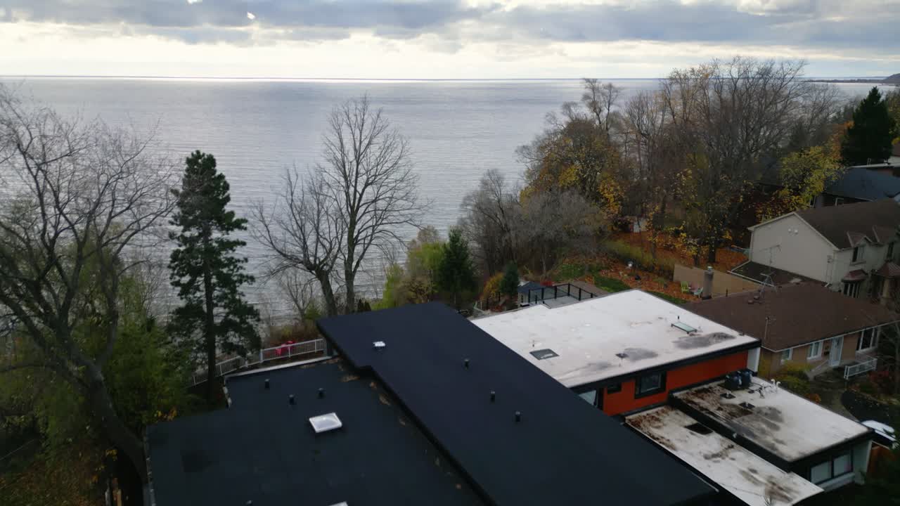 An overhead drone dolly over a residential neighborhood with sleek modern homes surrounded by trees calm peaceful lake views at sunset