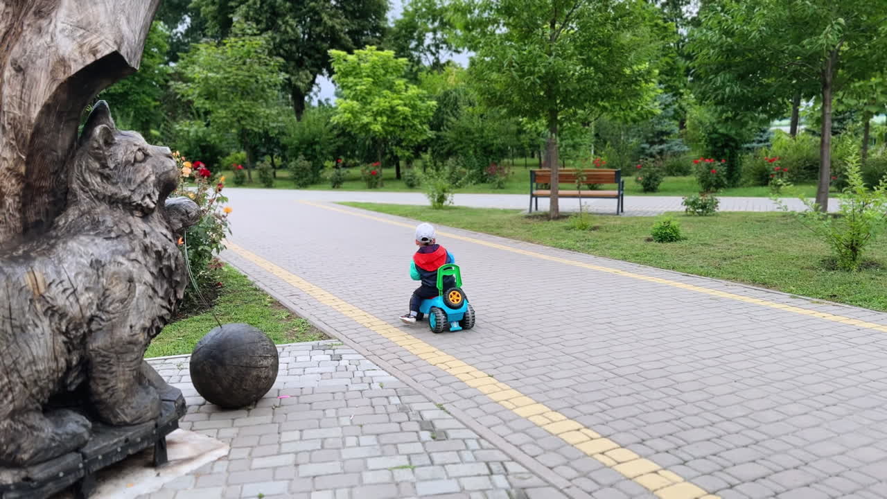 Caucasian baby boy riding a toy car outdoors. Little kid pushes from the ground to move quickly by the road in the park.