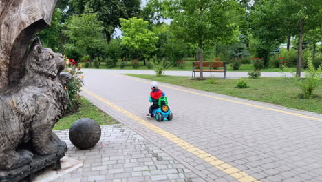 caucasian baby boy riding a toy car outdoors. little kid pushes from the ground to move quickly by the road in the park.