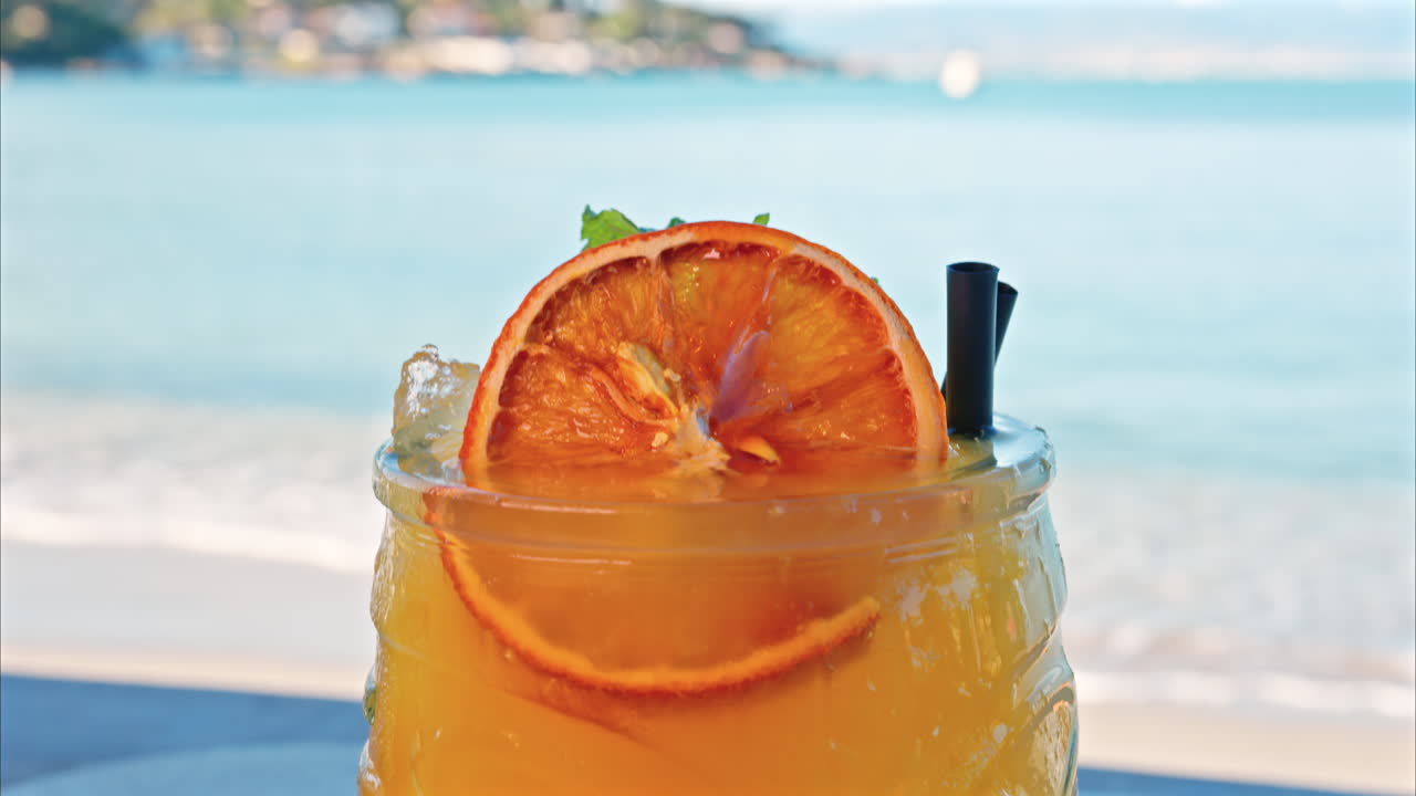 Close up of an orange cocktail on a table with a blurred view of the sea on the background