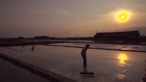 silhouette-of-two-workers-raking-the-salt-fields-in-south-east-asia