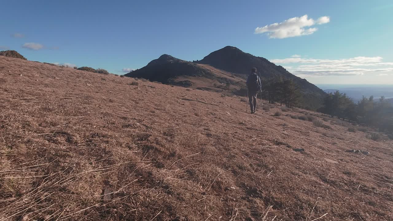 Vista di spalle di un giovane escursionista che cammina verso la montagna con bastoncini da trekking durante il tramonto con luce laterale nella catena montuosa della Sierra Norte di Madrid