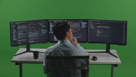 back view of asian man developer thinking about something while write code with multiple computer screens in green screen studio