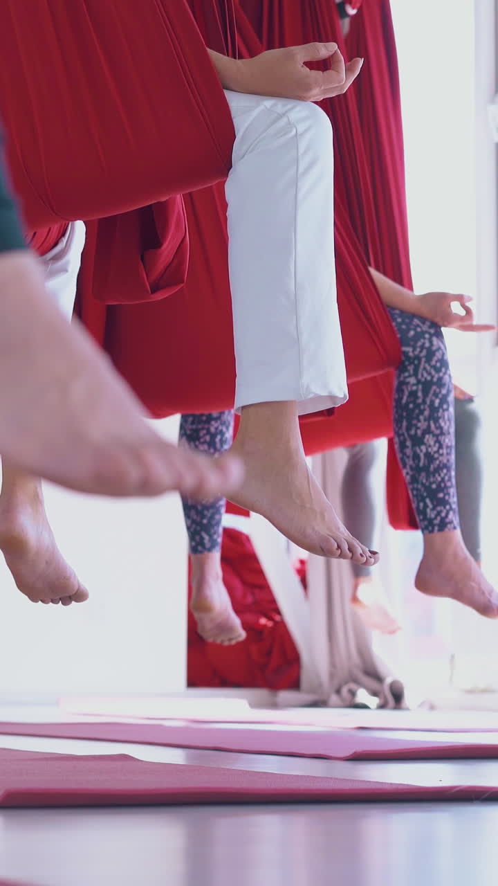 relaxed meditating women bare feet hang down from anti-gravity red hammocks in white room low angle shot close view