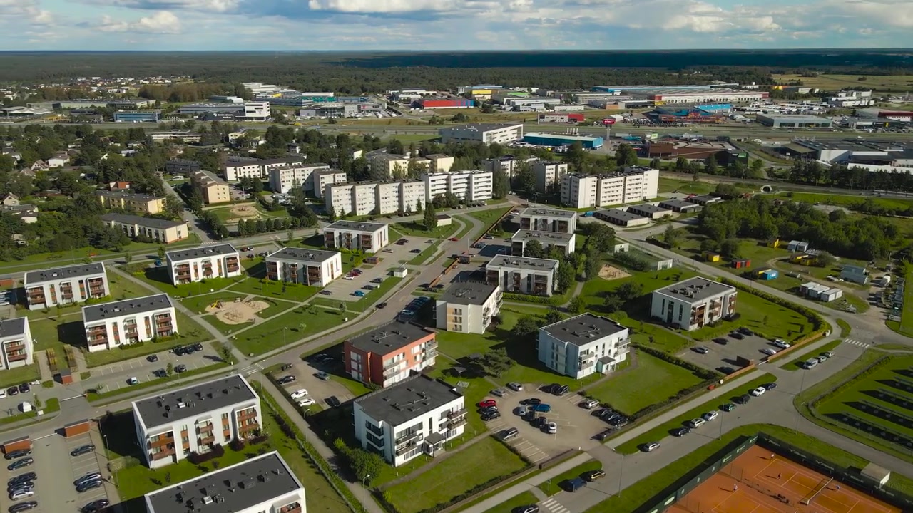 Flygvideo med drönare över ett modernt bostadsområde i Laagri alevik i Estland under en solig sommardag, med moderna lägenheter, synlig tennisbana och lokala småvägar mellan husen.