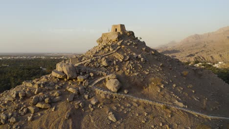 an aerial at sunset of dhayah fort in ras al-khaimah in the uae, flying over it, revealing the desert and emirates flag