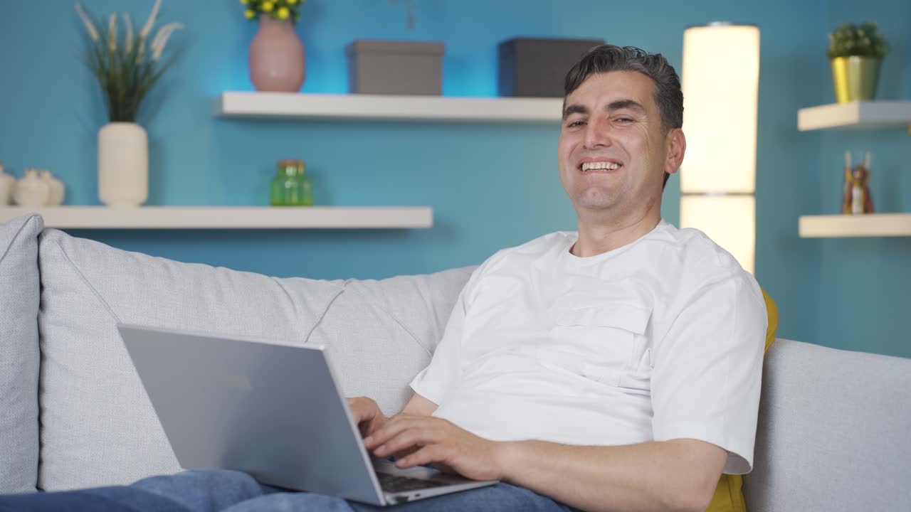 hombre trabajando en la computadora portátil mira a la cámara y se ríe. expresión relajada.