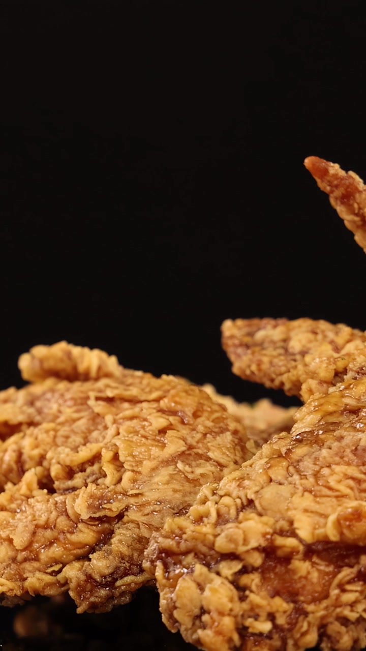 Sayap ayam goreng renyah keemasan berputar dengan mulus di bawah pencahayaan studio, menonjolkan tekstur renyah dan detail berair dengan latar belakang hitam tanpa sambungan dengan gerakan kamera lambat.