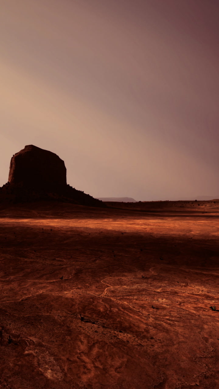 Desert landscape with a large rock formation under a colorful sky at dusk