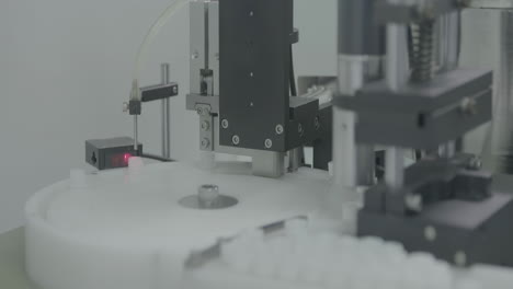 scientist operate vaccine capping process in automated pharmaceutical production line manufacturing, cap placing on vials of vaccine injections drugs in sterile surface in a laboratory setting.