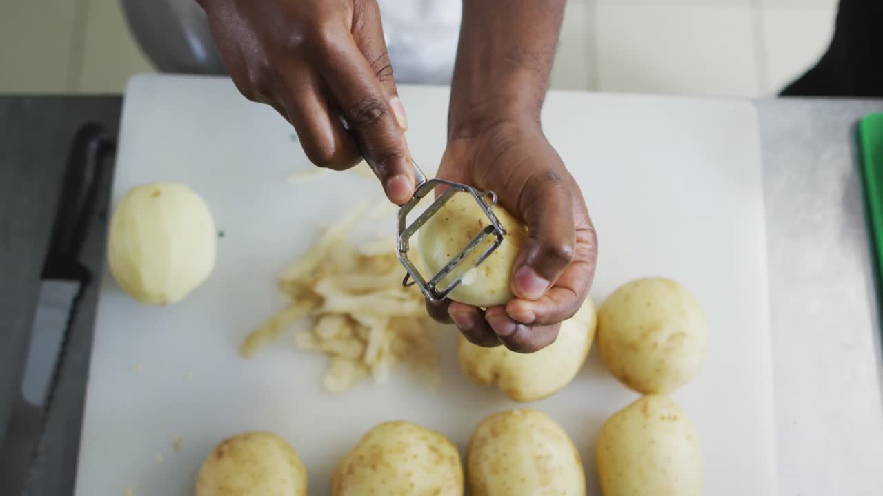 sección media de una chef afroamericana pelando patatas en la cocina de un restaurante