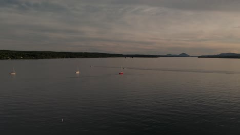 sunset view with small boats crossing the serene lake of memphremagog lying between magog, quebec, canada and newport, vermont, usa - extreme wide shot