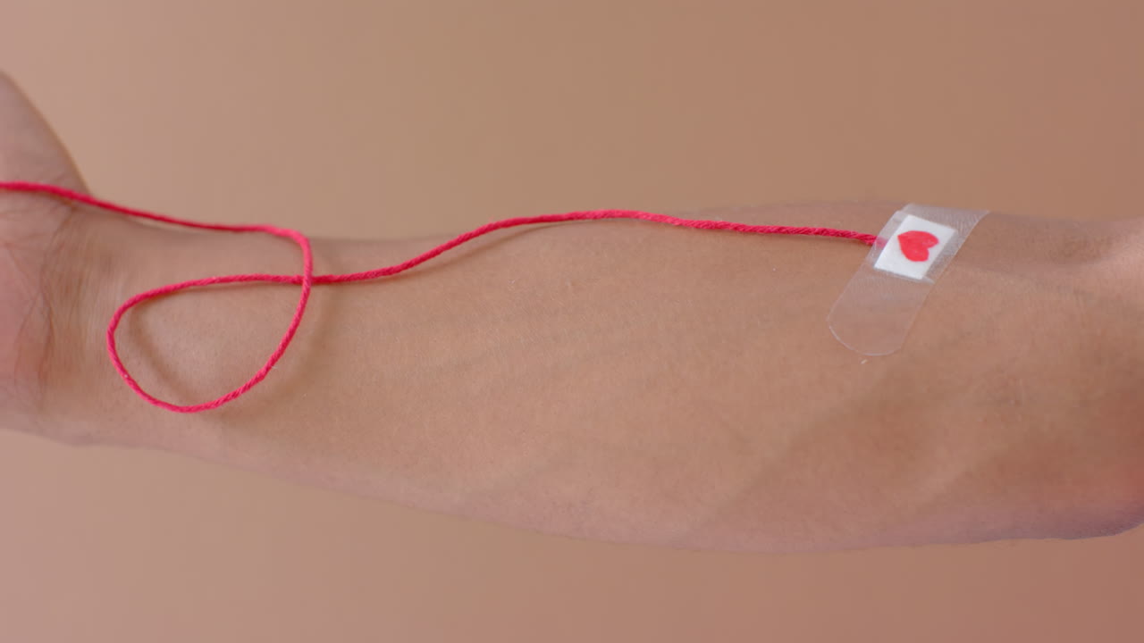 피 한 방울,  ⁇ 은  ⁇ 줄, 그리고 베이지색에 붙여진 심장 플라스처를 가진 두 인종 남자의 손, 느린 동작