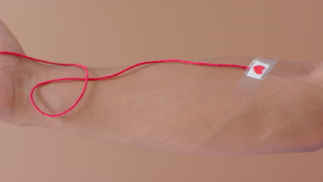 mano de hombre biracial con gota de sangre, cuerda roja y corazón pegando yeso en beige, cámara lenta