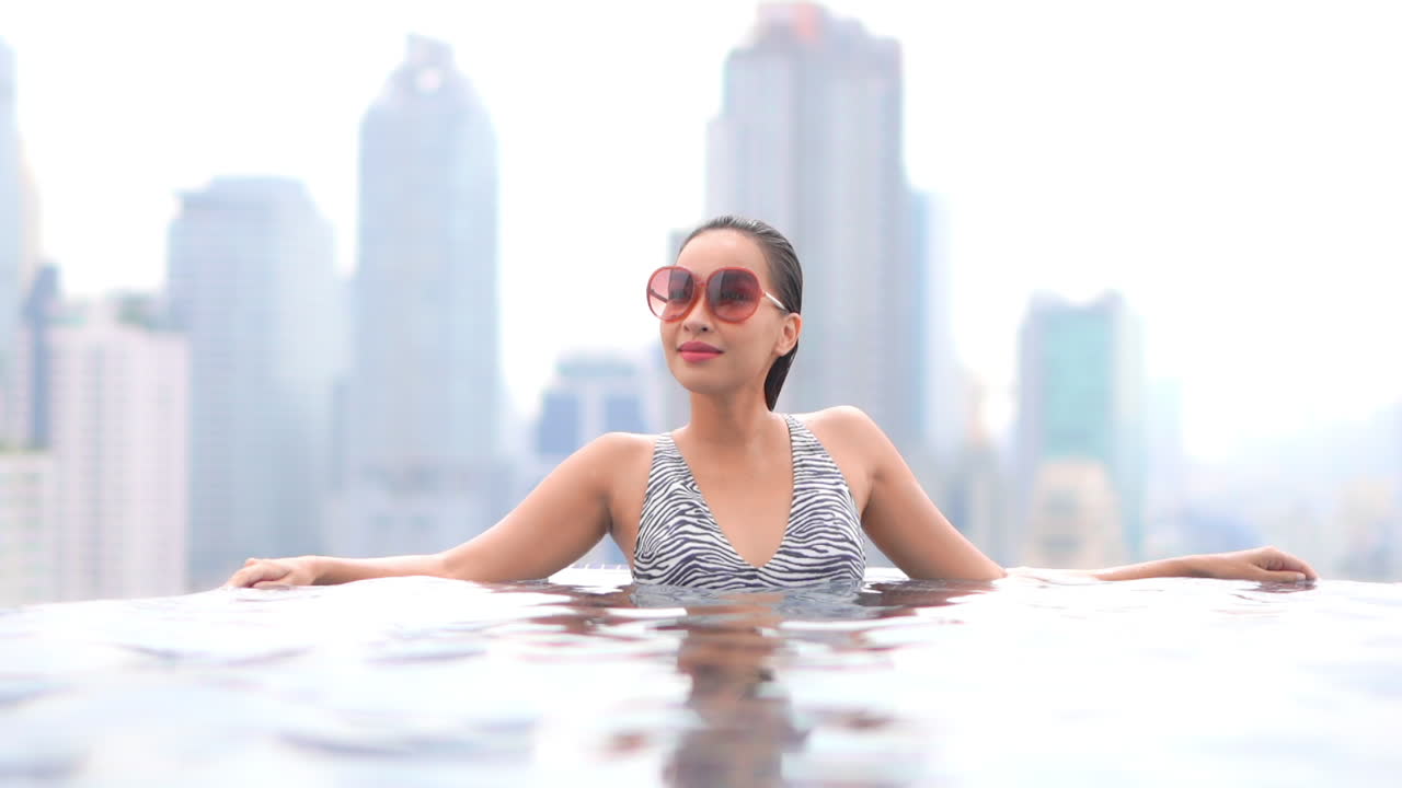 백그라운드에서 현대 대도시 도시와 옥상 수영장에서 섹시한 아시아 여자