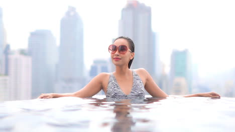 sexy asian woman in rooftop swimming pool with modern metropolis cityscape in background