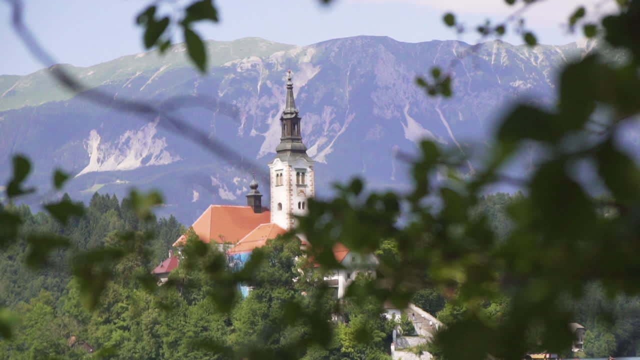 Chiesa della Madre di Dio sul lago di Bled tra il fogliame, panoramica a destra, slow motion