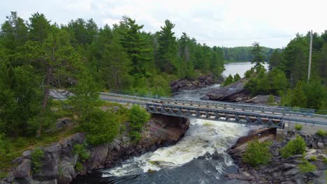 aerial drone shot following a fast flowing river surrounded by trees, passing above a motor vehicle bridge and into the magnetawan river, ontario, canada