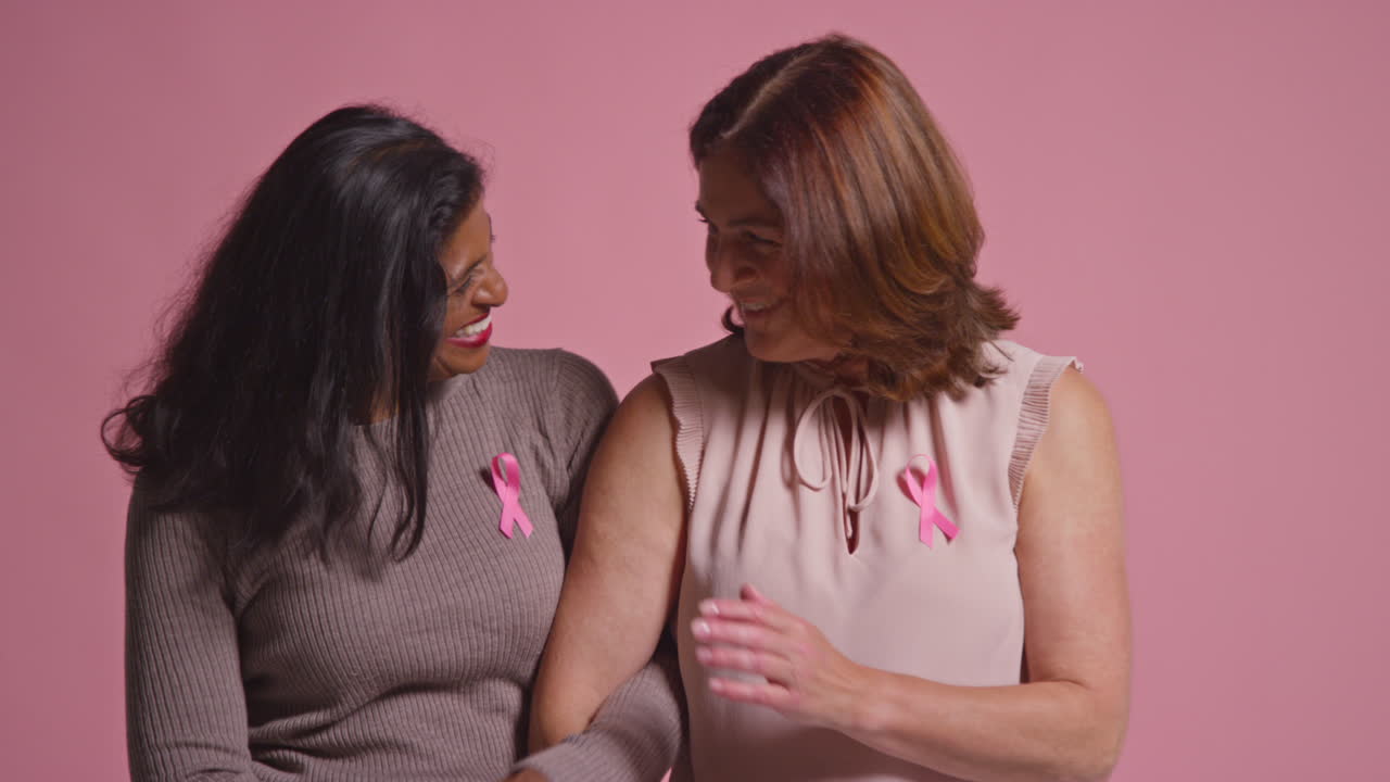retrato de estudio de dos mujeres maduras orgullosas de cintas rosadas de concienciación sobre el cáncer de mama abrazándose contra un fondo rosado 2