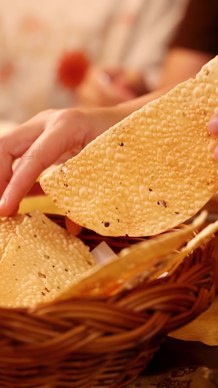 Close-up of hands selecting thin Indian flatbread from a basket under warm indoor lighting.