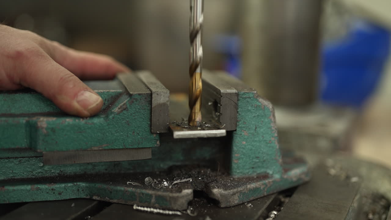 Drill bit penetrating a metal plate secured in a vise, high precision machining in an industrial workshop