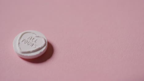 mano recogiendo caramelos de corazón con un mensaje romántico todo tuyo sobre fondo rosa