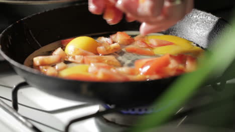 egg frying in a pan adding tomato slices